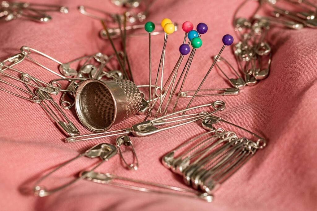 Close-up of colorful sewing pins, safety pins, and thimble on pink fabric.